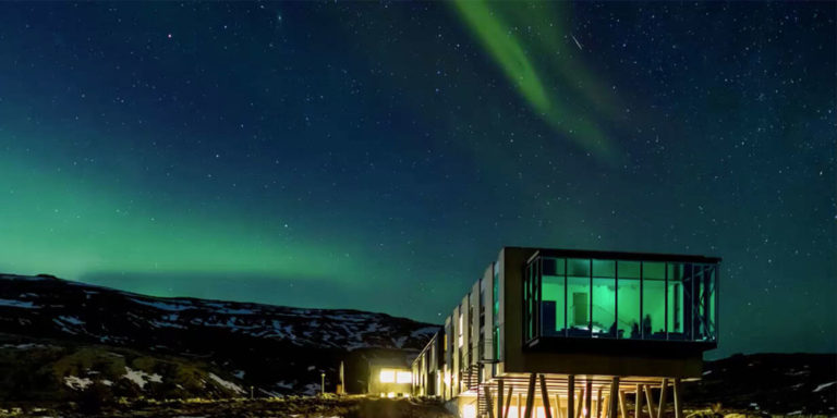 Luxury gay honeymoon: modern hotel with glass walls under the aurora borealis. Unusual travel destination for LGBTQ+ couples.