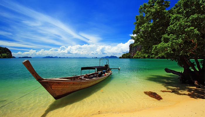 Longtail boat on a beach with clear water, blue sky, and lush greenery. Ideal gay travel destination for relaxation and adventure.