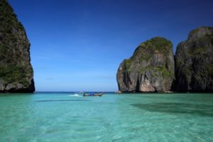 Maya Bay, Thailand. Tropical beach with limestone cliffs, clear turquoise water, and a boat. A gay travel destination.