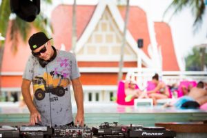 TropOut DJ at a gay pool party. Man with headphones playing music on Pioneer equipment. Gay travel, events, and parties.