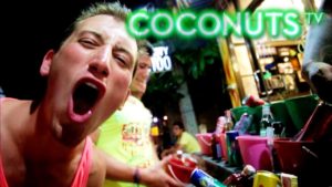 Gay travel advice: A man with his mouth open in a bar setting. Coconuts TV logo visible. Nightlife scene, possibly in a gay-friendly destination.