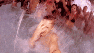 Gay pool party scene: Man in water with hand over face, surrounded by other partygoers. Fun gay travel destination.