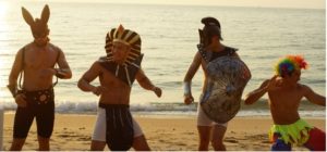 Four gay men in costumes on a beach. Best beach party outfit: bunny ears, Egyptian pharaoh, gladiator, and clown. Fun gay travel.