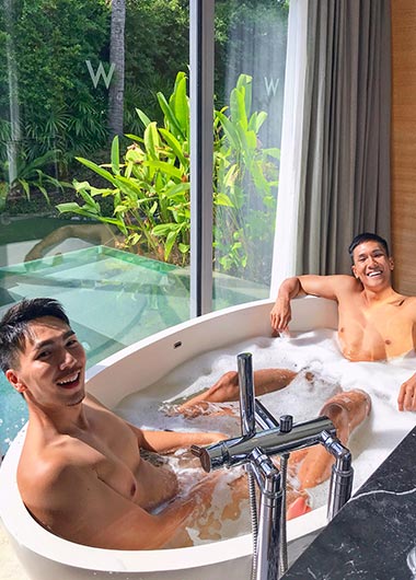 Two gay men relax in a bubbly bathtub at W Samui Hotel, Thailand. Luxury gay-friendly travel and vacation experience.