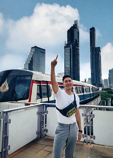 Gay man in Bangkok points up, with BTS Skytrain & Sathorn skyline. Holiday Inn Express is a gay-friendly hotel in central Bangkok.