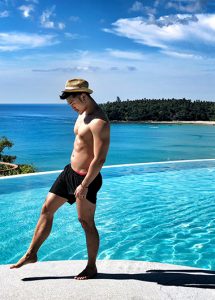 Gay-friendly The SIS Kata Resort Phuket infinity pool view. Man in swim trunks & hat. Best hotel for gay travel. Thailand vacation.
