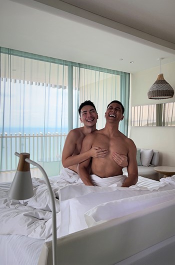 Gay honeymoon at Hilton Pattaya. Two shirtless men, wrapped in towels, laugh in a hotel room with a sea view. A great gaycation choice.
