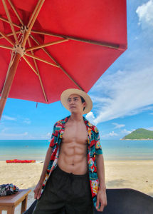 Gay traveler at Anantara Rasananda Koh Phangan Villas, a beachfront resort with private pool villas. Man on beach under red umbrella.