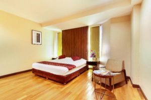 Bally Suite Silom, a gay-friendly hotel room. Features a bed with red accents, a chair, and wooden floors. Modern design for gay travelers.