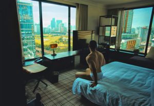 Gay-friendly Grand Hyatt Erawan Bangkok hotel room view. Man sits on bed. Bangkok skyline outside window. Gay travel advice.