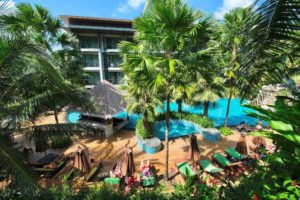 Hula Hula Resort Ao Nang, a gay-friendly hotel. View of the pool area with palm trees, sun loungers, and a bar. A tropical paradise.