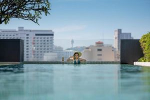 Page 10 Hotel's rooftop pool view. Woman in hat enjoys the infinity pool overlooking the cityscape. Gay-friendly hotel travel.