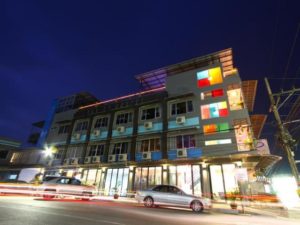 Exterior nighttime view of Pak Up Hostel, a gay-friendly hotel. Building features colorful windows and modern design. Travel advice for gay men.