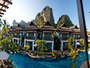 Railay Village Resort, a gay-friendly hotel. Thai-style bungalows surround a pool with mountains in the background. Ideal for gay men travel.
