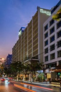Exterior of Tawana Bangkok Hotel at dusk. Gay-friendly hotel in Bangkok, Thailand. Street view with light trails from cars.