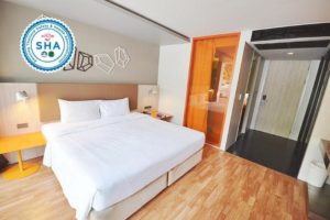 The Heritage Silom Hotel room. Gay-friendly hotel bedroom with king bed, wood floors, and orange accents. SHA certified for safety.