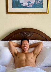 Shirtless man relaxing in bed at Sofitel Krabi Phokeethra Golf and Spa Resort. Instagram-perfect beach resort for gay travel.