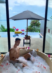Gay Koh Samui Hotel: Man relaxing in a bubble bath with champagne. Infinity pool and unicorn float in the background at Conrad Hotels.