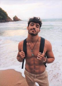 Instagram-worthy gay man at Ao Nang Beach, Krabi. Perfect beach holiday style at Krabi Holiday Inn Resort. Backpack, jewelry, tan, abs.