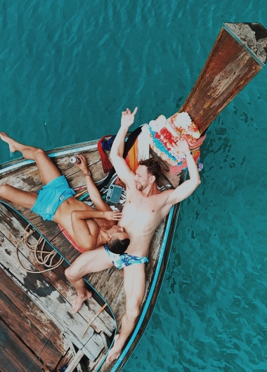 Gay honeymoon at SAii Phi Phi Island Village. Two men relax on a longtail boat in Thailand's turquoise waters. Perfect gay travel destination.