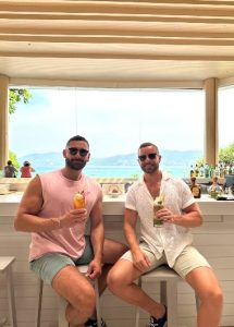 Gay honeymooners at Amari Phuket, Thailand. Two men enjoy cocktails at a beachfront hotel bar with ocean views. Top gay honeymoon destination.