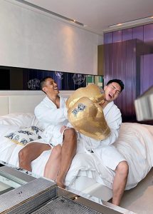 Two gay men in robes playfully boxing with gold gloves at W Bangkok, a top gay hotel near Silom gayborhood. Bangkok gay travel.
