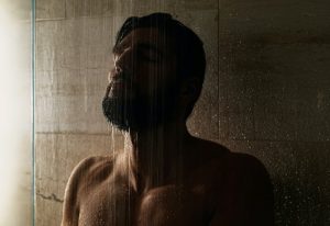Bearded man under shower in a Bangkok gay sauna. Dark, moody lighting. Relaxation and cleanliness. Gay travel.