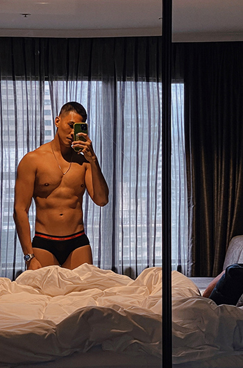 Shirtless man takes a selfie in a mirror at Pullman Sydney Hyde Park hotel. Gay hotel with rooftop pool. Luxury travel for gay men.