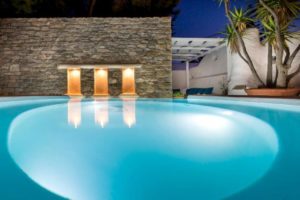 Carbonaki Hotel's pool at night. Gay-friendly hotel with lit wall alcoves reflecting in the water. Serene Mykonos travel for gay men.