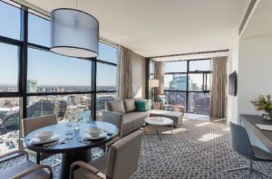Fraser Suites Sydney: Gay-friendly hotel room with city view. Dining table, sofa, and desk in a modern suite. Great for gay travel in Sydney.