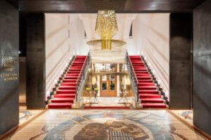 Grand entrance of Mosaic House Design Hotel, a gay-friendly hotel. Red carpeted stairs, mosaic floor, and modern chandelier.