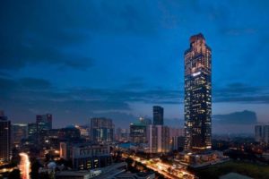 Night view of The Westin Jakarta, a gay-friendly hotel. The Jakarta skyline features illuminated skyscrapers against a dark blue sky.