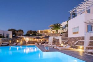 Vencia Boutique Hotel's pool at dusk. A gay-friendly hotel with a bar, lounge chairs, and white buildings on a hill in Mykonos, Greece.