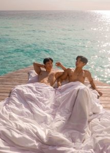 Gay couple relaxes in bed on a dock at Centara Ras Fushi Resort & Spa, Maldives. KelvinMark photo. Gay travel advice.