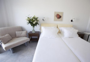 Marisso Hotel Mykonos Town room. Budget gay hotel in gayborhood, features twin beds, a couch, flowers, and a seashell picture. Clean, modern.