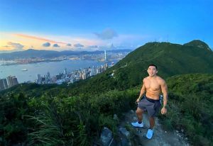 Gay Hong Kong travel: Shirtless man hiking, showcasing Hong Kong's skyline. Best hiking spots for gay travelers in Hong Kong. Outdoor adventure.