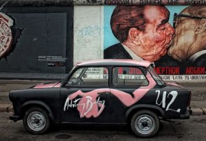 Gay Berlin travel: Trabant car with Achtung Baby art parked by the East Side Gallery's Fraternal Kiss mural. Gay travel Berlin.
