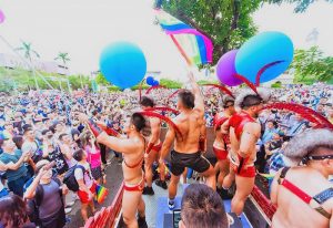 Gay Pride Taipei: A vibrant crowd celebrates. Men on a float wave rainbow flags and balloons. Gay travel guide info.