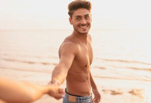 Gay Bali Travel Guide: Shirtless man holds hand on beach. Bali is a popular destination for gay men and travel.