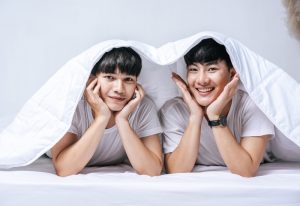 Two beloved young men sleep in bed together under a blanket. Gay couple at a Beijing hotel. Gay travel advice.