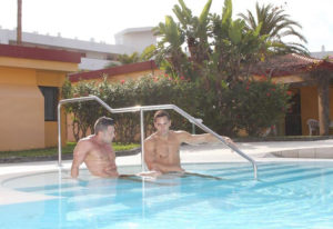 Bungalows Tenesoya gay men only hotel pool in Gran Canaria near Yumbo Center. Two shirtless men relaxing in the water on vacation.