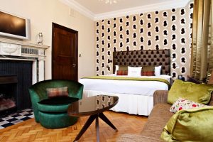 Courthouse Hotel's gay-friendly, pet-friendly room. Features a bed, sofa, chair, fireplace, and unique wallpaper. Ideal for gay travel.