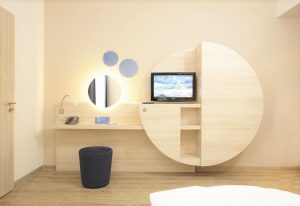H2 Hotel Berlin-Alexanderplatz room. Modern design with desk, TV, round mirror, and stool. Gay-friendly hotel for your Berlin visit.
