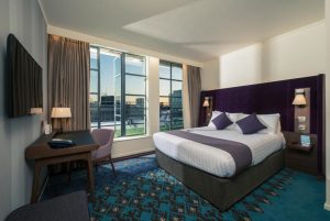 Mercure London Bridge gay-friendly hotel room. Modern design with large windows, purple accents, desk, and patterned carpet. Comfortable stay.