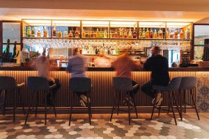 Qbic London City hotel bar. People sit at the bar with drinks. Gay-friendly, pet-friendly hotel in London. Interior design with bottles and glasses.
