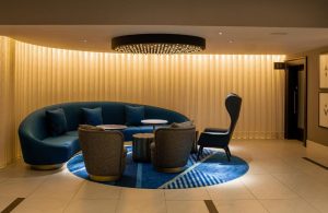Strand Palace Hotel's stylish lounge area. Modern design with blue sofa, armchairs, and unique lighting. A gay-friendly hotel choice.