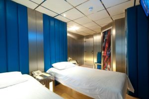 Stylotel, a gay-friendly hotel: Twin beds with white linens, blue padded wall panels, and metallic accents. Modern design for gay travelers.