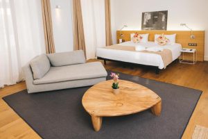Zenit Budapest Palace gay-friendly hotel room. Modern interior with bed, couch, wooden table, and stylish decor. Ideal for gay travel in Budapest.