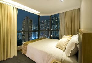 Bedroom at Bishop Lei International House, a gay-friendly hotel in Hong Kong, with a city view at night. Hotel room interior.