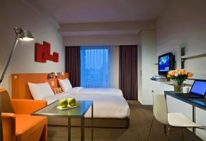 Gay-Friendly Citadines Shinjuku Hotel room with twin beds, orange accents, desk, and city view. Ideal for gay travelers in Shinjuku, Tokyo.